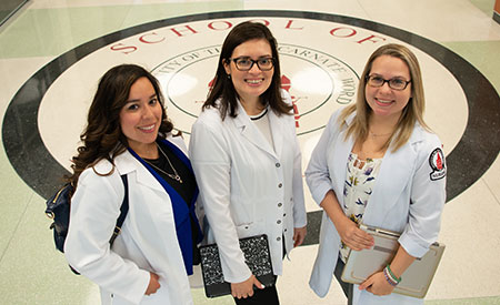 3 female nursing students smiling in white lab coats