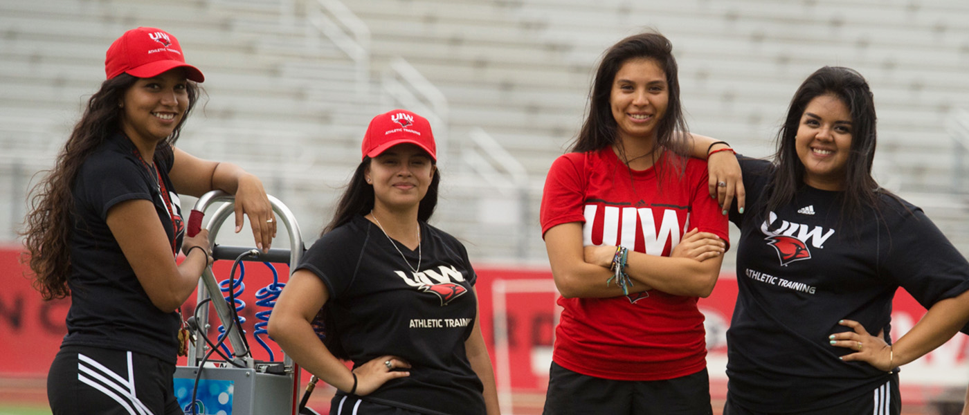 Four UIW Students posing with UIW clothing at the football field