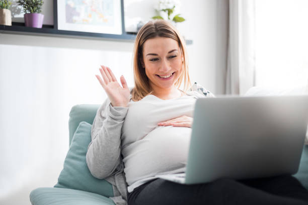 A pregnant woman waving hello to her laptop