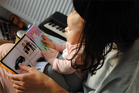 A mother holding her baby as they read a toddler book